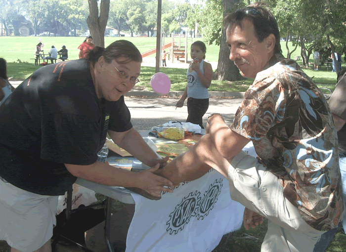 Photo de Marianne Hladun appliquant un tatouage sur la jambe de Larry Hubich, pr&eacute;sident de la F&eacute;d&eacute;ration du travail de la Saskatchewan